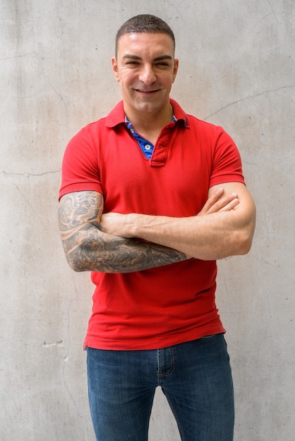 Happy handsome man smiling with arms crossed against concrete wall