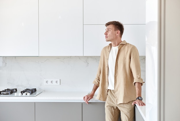 Happy handsome man standing on minimalistic kitchen and smiling