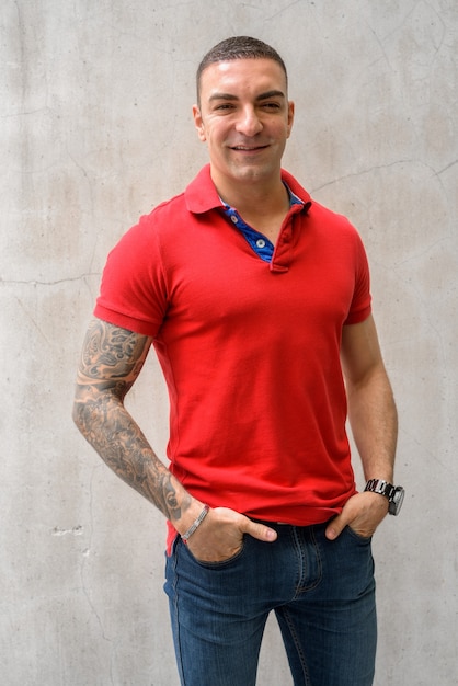 Happy handsome man with tattoos smiling against concrete wall