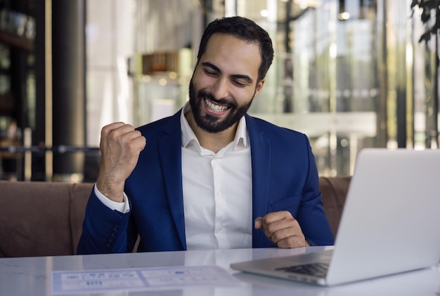 Happy handsome Moroccan trader receive payment celebration success in modern office