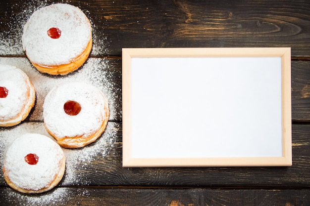 Happy Hanukkah Empty frame for congratulations text and traditional dessert Sufganiyot on dark wooden background Celebrating Jewish holiday