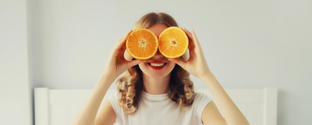 Photo happy healthy cheerful young woman covering her eyes with slices of orange fruits and looking for