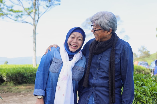 Happy and healthy elderly couple laughing at tea plantation Old man hugging and looking his wife