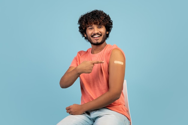 Happy hindu guy pointing at medical band on his shoulder