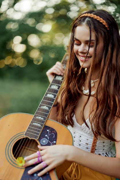 Happy hippie woman with a guitar relaxing in nature sitting on a plaid smiling and enjoying the view Lifestyle in harmony with nature and self High quality photo