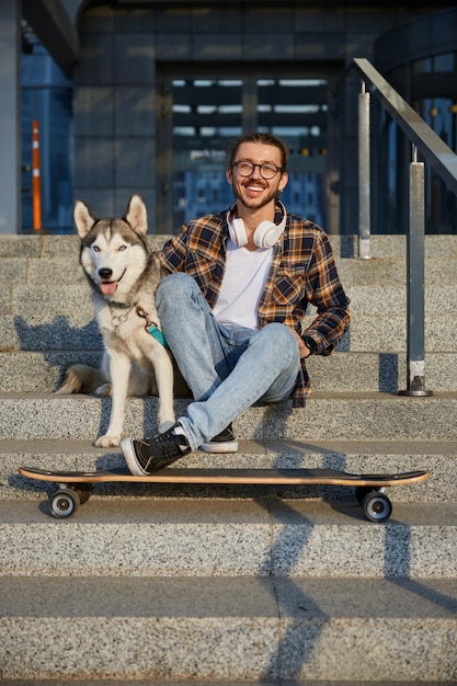 Happy hipster gay skateboarder resting and sitting with loving dog