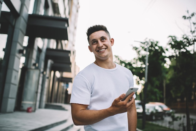 Happy hipster guy in casual tshirt with copy space for brand standing at urban setting and laughing