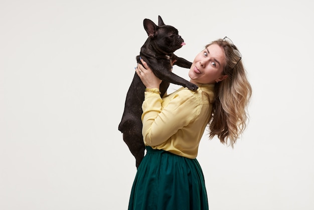  Happy hipster woman playing with french bulldog on white wall