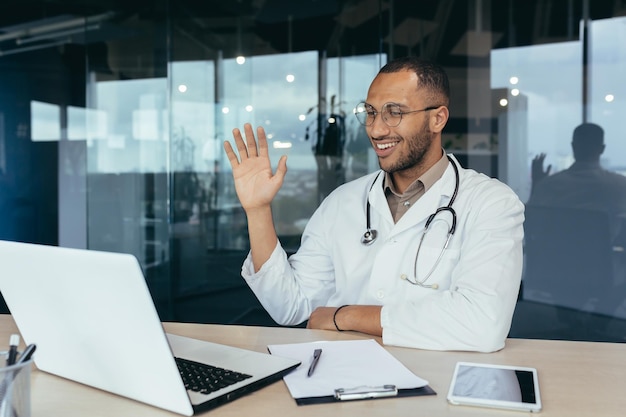 Happy hispanic doctor smiling and talking on video call man in white coat and stethoscope using