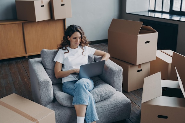 Happy hispanic woman renting apartment online Homeowner is sitting in armchair with pc