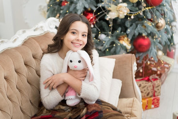 Happy holiday. happy new year mood. happiness and joy. ready for xmas presents. small girl love her bunny. best christmas toy. cheerful kid play toy at christmas tree. feeling cosy at home.