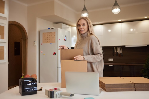 Happy homeowner renter girl using laptop at pile of stacked boxes ordering delivery shipping transpo