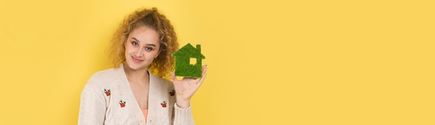 Happy house buyer A young girl holds a model of a green house in her hands The concept of green energy ecology