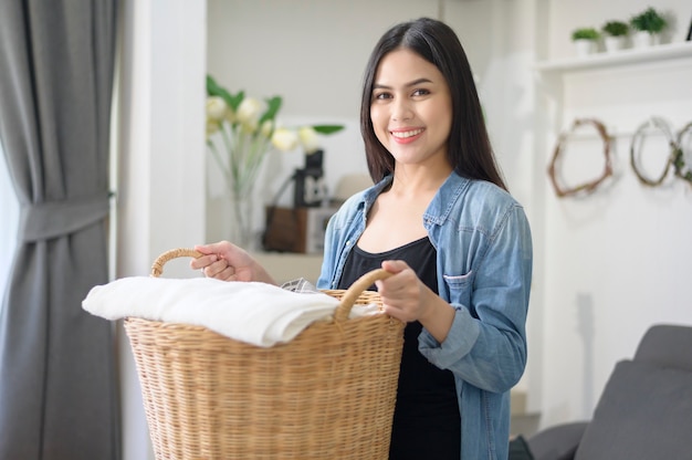 A happy housekeeper is carrying a bucket cloths for laundry in the house.