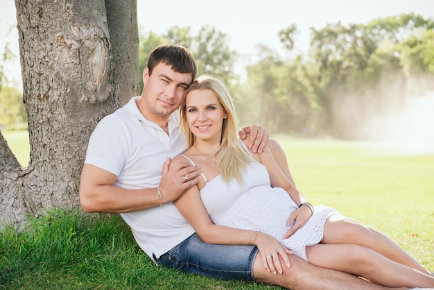 Happy husband hug his pregnant wife. Family rest on open-air under the tree