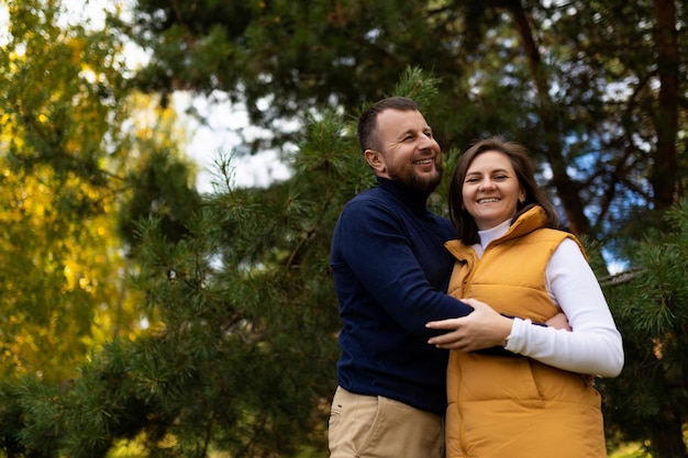 A happy husband joyfully hugs his wife against the backdrop of an autumn forest