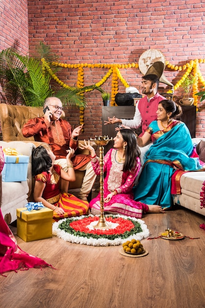 Happy Indian Family Celebrating Ganesh Festival or Chaturthi  Welcoming or performing Pooja and eating sweets in traditional wear at home decorated with Marigold Flowers