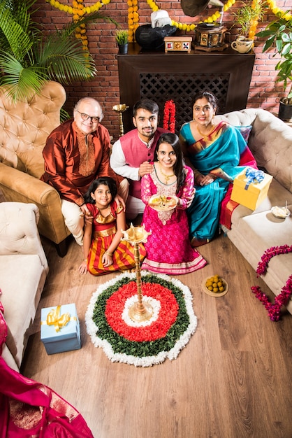 Happy Indian Family Celebrating Ganesh Festival or Chaturthi  Welcoming or performing Pooja and eating sweets in traditional wear at home decorated with Marigold Flowers