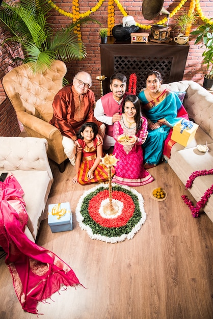 Happy Indian Family Celebrating Ganesh Festival or Chaturthi  Welcoming or performing Pooja and eating sweets in traditional wear at home decorated with Marigold Flowers