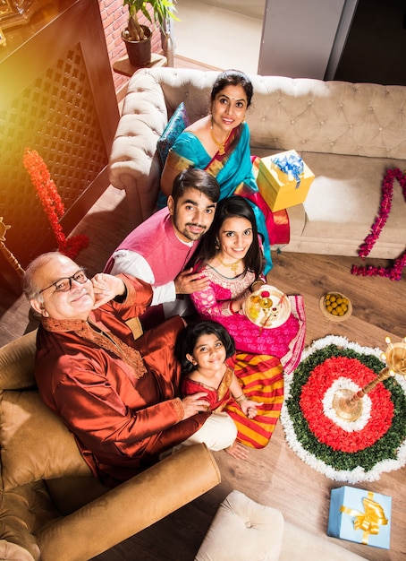 Happy Indian Family Celebrating Ganesh Festival or Chaturthi  Welcoming or performing Pooja and eating sweets in traditional wear at home decorated with Marigold Flowers