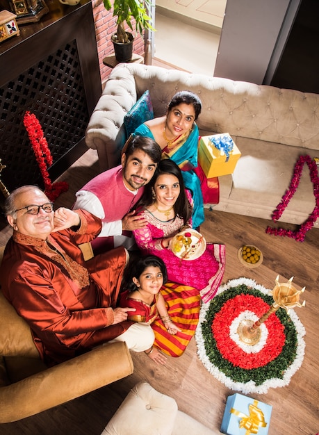 Happy Indian Family Celebrating Ganesh Festival or Chaturthi  Welcoming or performing Pooja and eating sweets in traditional wear at home decorated with Marigold Flowers