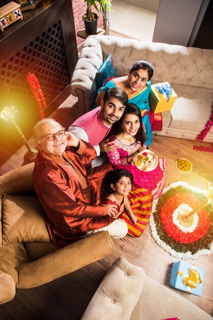 Happy Indian Family Celebrating Ganesh Festival or Chaturthi  Welcoming or performing Pooja and eating sweets in traditional wear at home decorated with Marigold Flowers