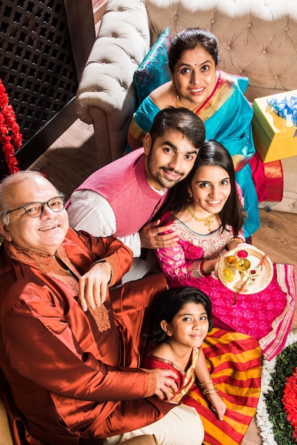 Happy Indian Family Celebrating Ganesh Festival or Chaturthi  Welcoming or performing Pooja and eating sweets in traditional wear at home decorated with Marigold Flowers