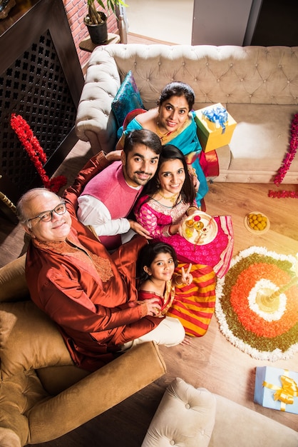 Happy Indian Family Celebrating Ganesh Festival or Chaturthi  Welcoming or performing Pooja and eating sweets in traditional wear at home decorated with Marigold Flowers