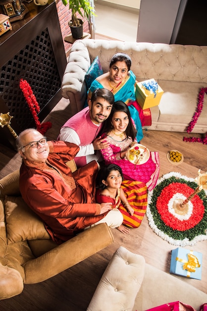 Happy Indian Family Celebrating hindu Festivals  Welcoming or performing Pooja and eating sweets in traditional wear at home decorated with Marigold Flowers