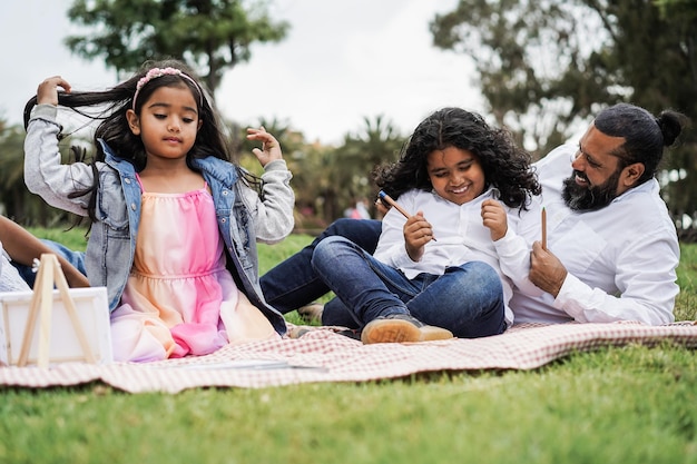 Happy indian family having fun painting with children outdoor at city park  Focus on boy hands