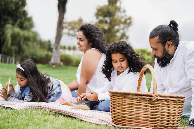 Happy indian family having fun painting with children outdoor at city park  Focus on father ear