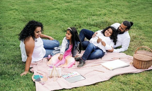 Happy indian family having fun painting with children outdoor at city park  Focus on father face