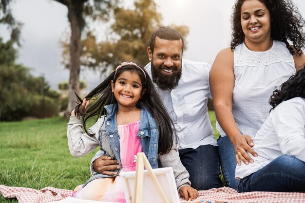 Happy indian family having fun painting with children outdoor at city park - Main focus on girl face