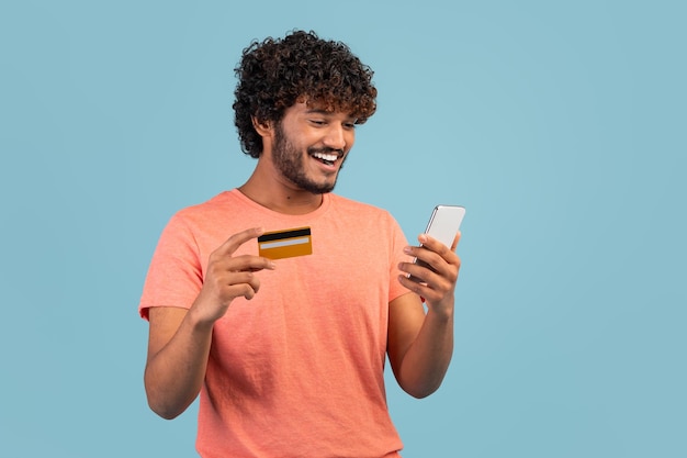 Happy indian guy holding cell phone and credit card