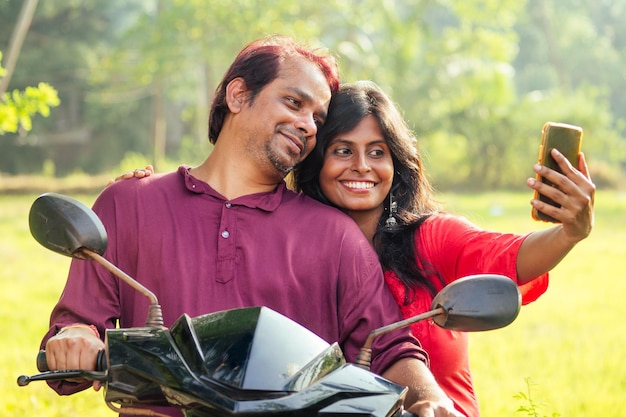 Happy indian married couple riding on motorbike in tropical jungle in Goa India