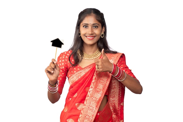 Happy Indian traditional young girl holding a little house cutout board in her hands on a white background