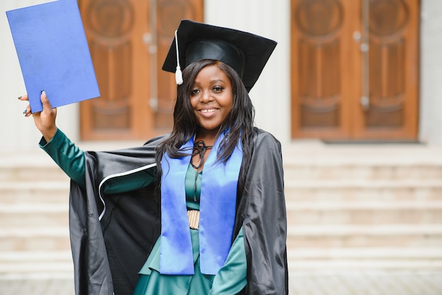 Happy Indian university student in graduation gown and cap holding diploma certificate. Portrait of mixed race Asian Indian and African.