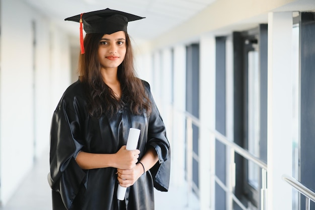 Happy Indian university student in graduation gown and cap holding diploma certificate