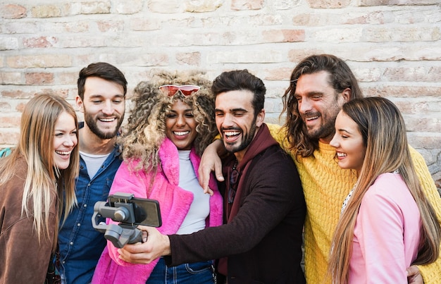 Happy influencer friends having fun vlogging with gimbal and mobile phone outdoor - Focus on right man face