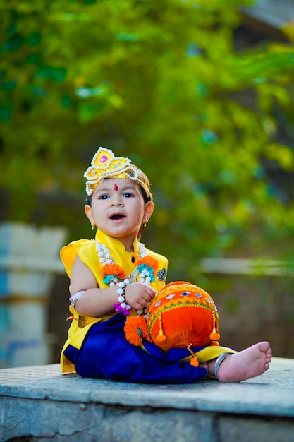 Happy Janmashtami Greeting Card showing Little Indian boy posing as Shri krishna or kanha/kanhaiya with Dahi Handi picture and colourful flowers.