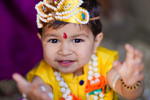 Happy Janmashtami Greeting Card showing Little Indian boy posing as Shri krishna or kanha/kanhaiya with Dahi Handi picture and colourful flowers.