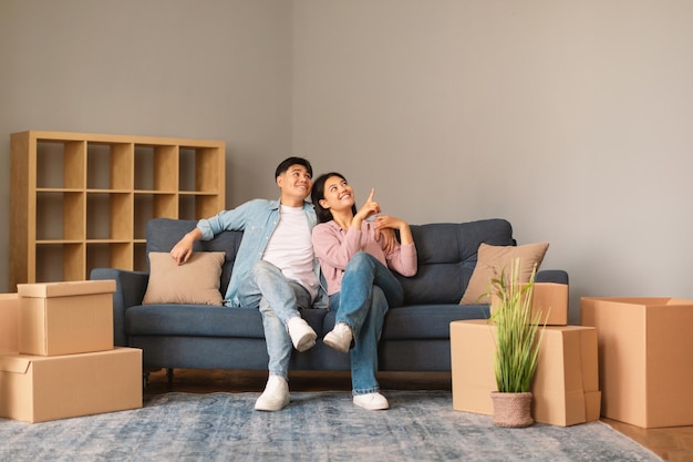 Happy japanese young spouses after moving sitting on sofa indoor