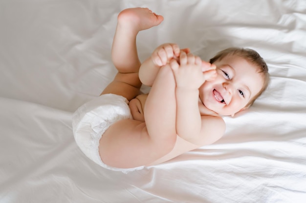 Happy joyful baby in diapers lying on white bed High quality photo