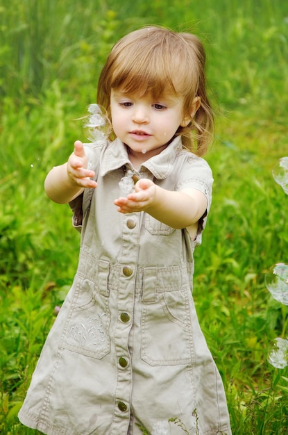 Happy joyful child girl on a sunny summer day against the background of nature and soap bubbles