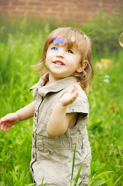 Happy joyful child girl on a sunny summer day against the background of nature and soap bubbles