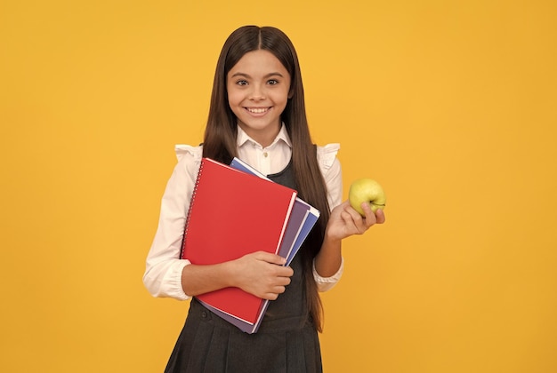 Happy kid back to school holding apple and books yellow background education