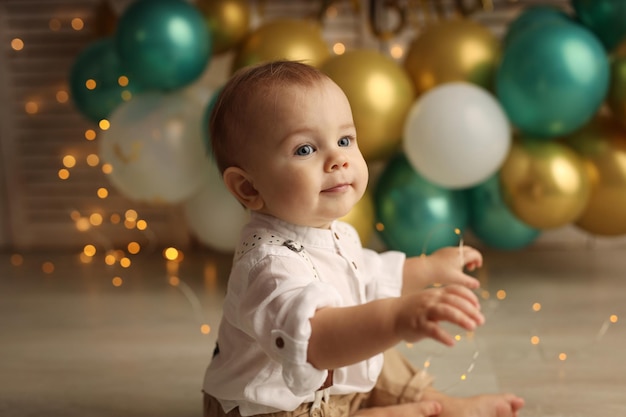 A happy kid on the background of balloons with garlands celebrates his birthday