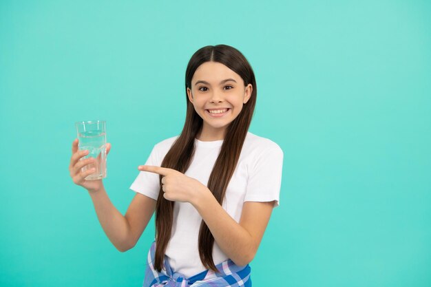 Happy kid drink glass of water to stay hydrated and keep daily water balance pointing finger