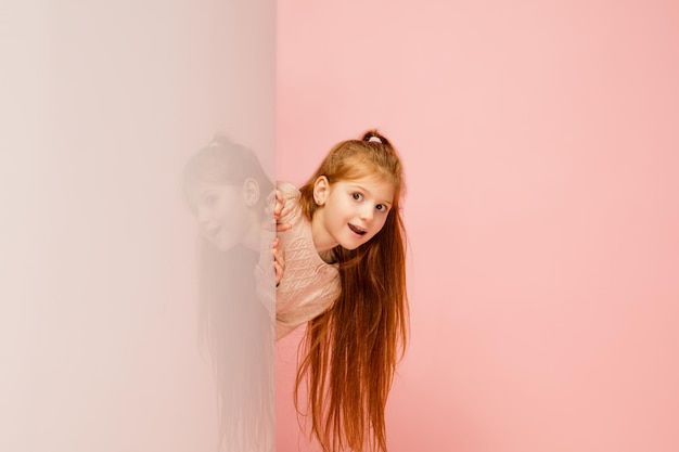 Happy kid girl isolated on coral pink studio background looks happy cheerful sincere copyspace