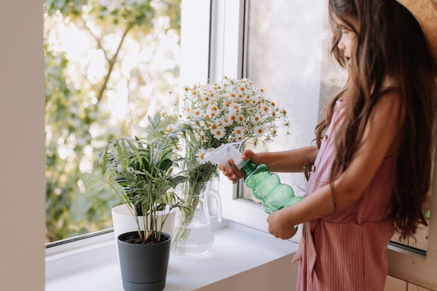 Happy kid girl taking care of houseplants at home dressed in stylish dusty pink outfit